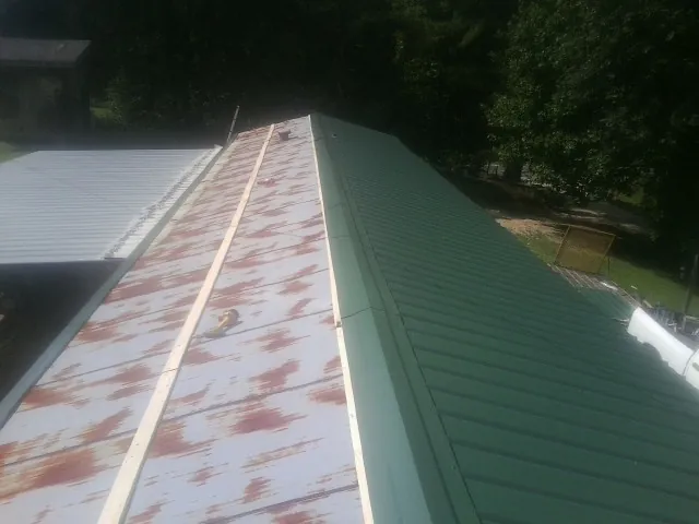 Old rusted panels beside newly installed green metal roofing — Wind Damage Roof Repair by Roofing Brothers in Hinckley
